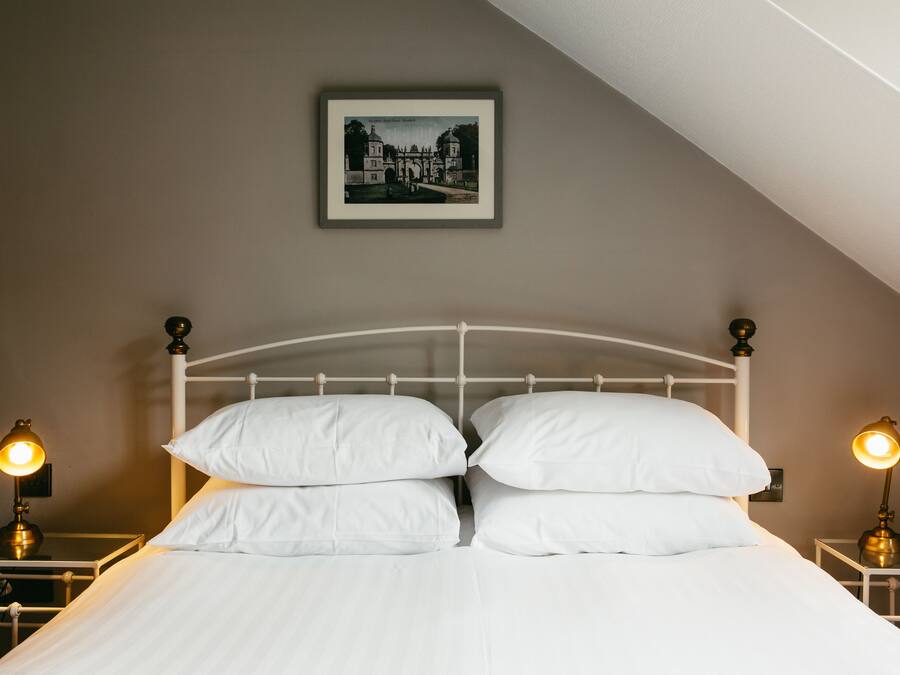 A neatly made bed with white linens and two bedside lamps.