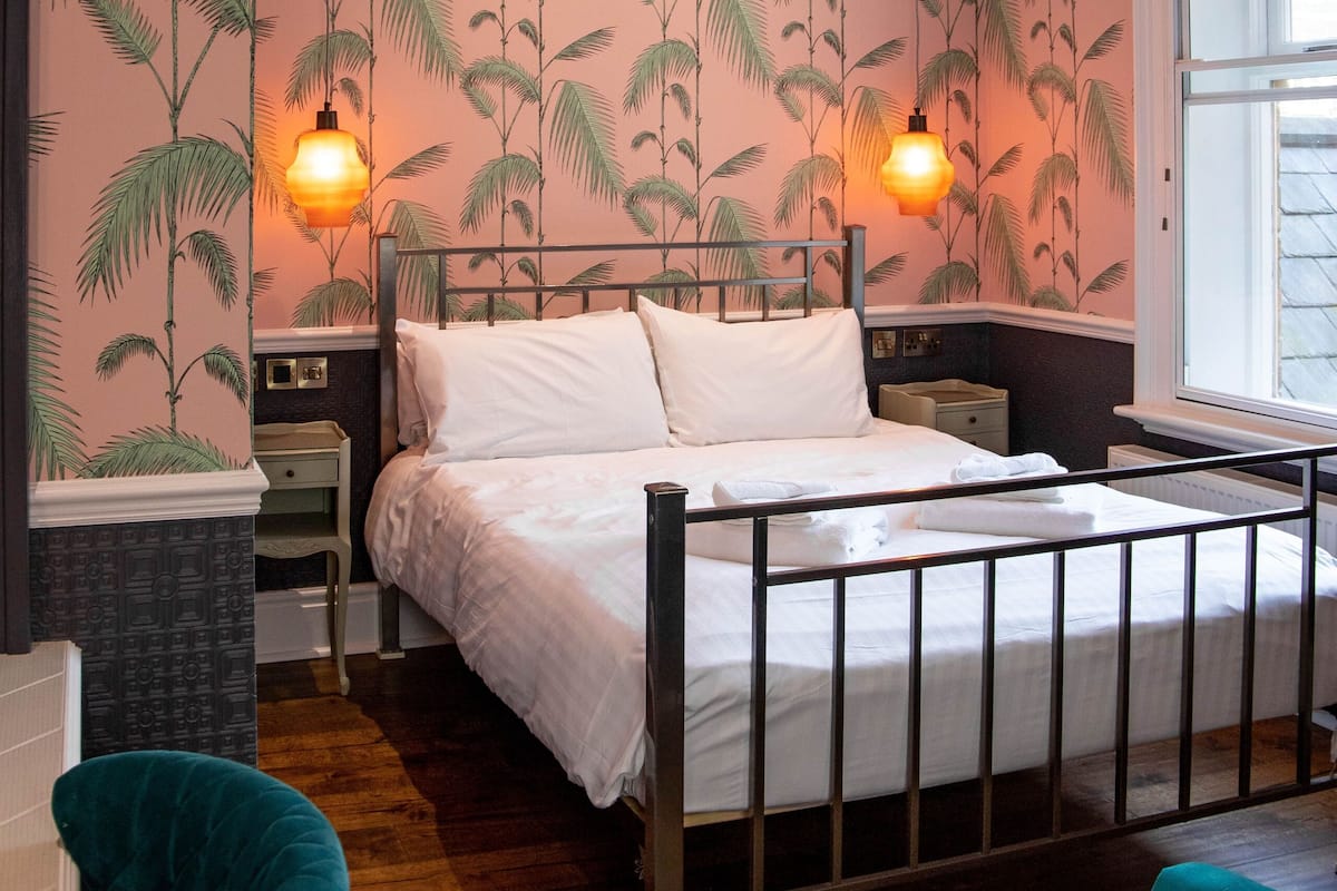 Een slaapkamer met een bed, een plafondventilator, twee wandlampen, een raam en een nachtkastje.