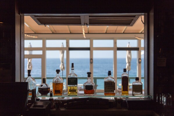 A bar area with various liquor bottles and a view of the ocean through large windows. - Pacific Edge Hotel (Laguna Beach)