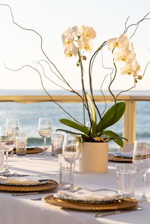A table set for dining with white orchids, clear glasses, and plates, overlooking a body of water. - Pacific Edge Hotel (Laguna Beach)