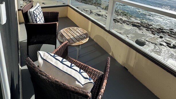Een balkon met rieten meubilair, een tafeltje en uitzicht op het strand en de zee.