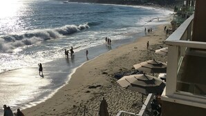 Een strand met mensen die langs de kust wandelen, parasols en uitzicht op de oceaan.