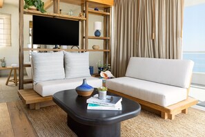 A modern living room with a sofa, a coffee table with books, a TV, and a view of the sea. - Pacific Edge Hotel (Laguna Beach)