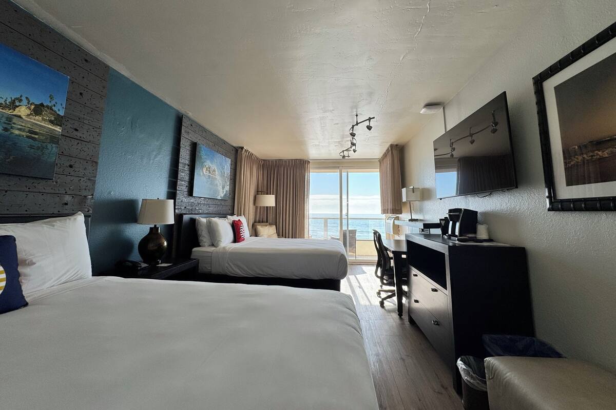 Une chambre d’hôtel avec deux lits, un bureau, une chaise, une télévision et une vue sur l’océan.