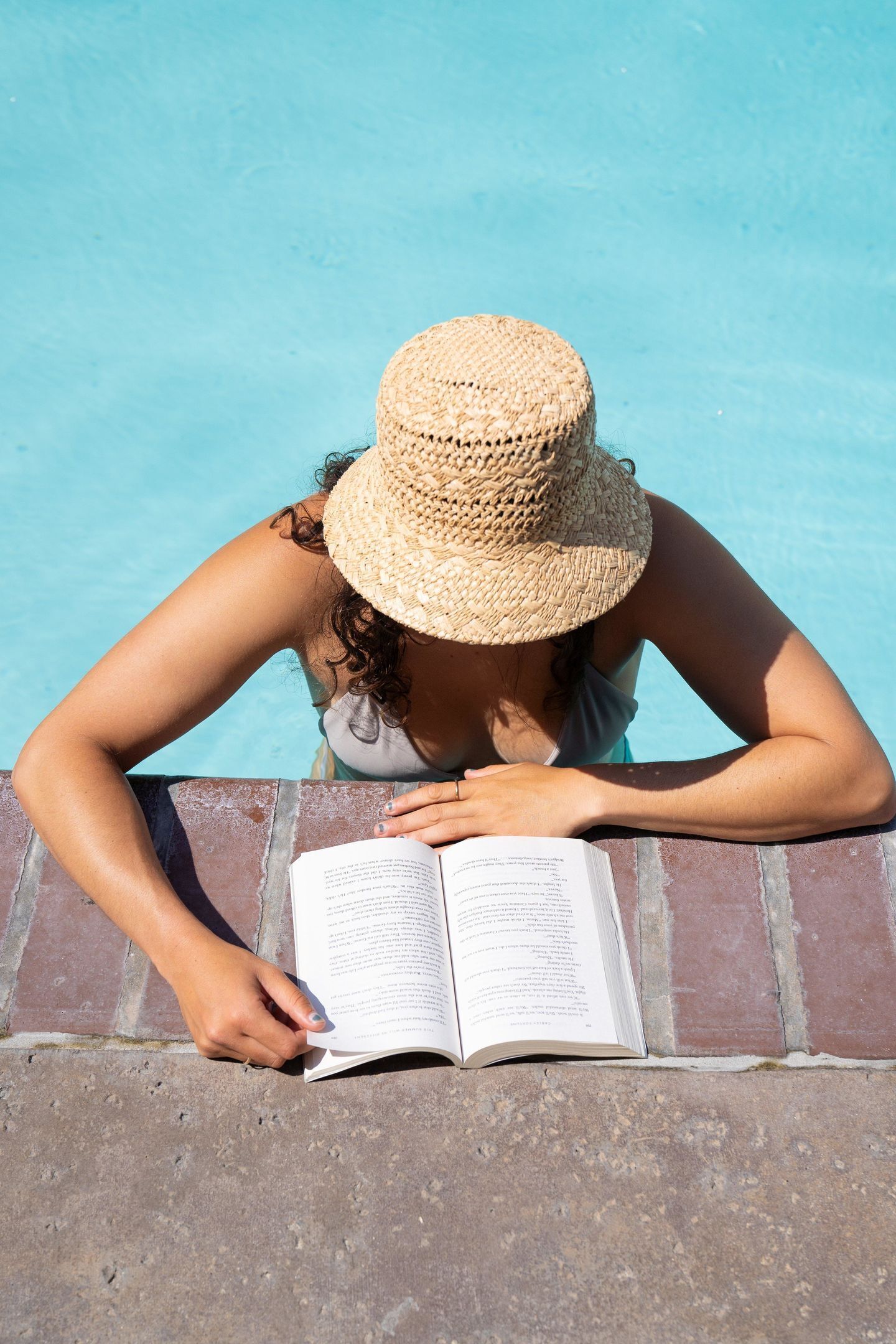 A person reading a book by a poolside.