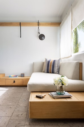Un salon minimaliste comprenant un canapé, une table basse avec un vase de fleurs, une lampe et une fenêtre avec des rideaux.