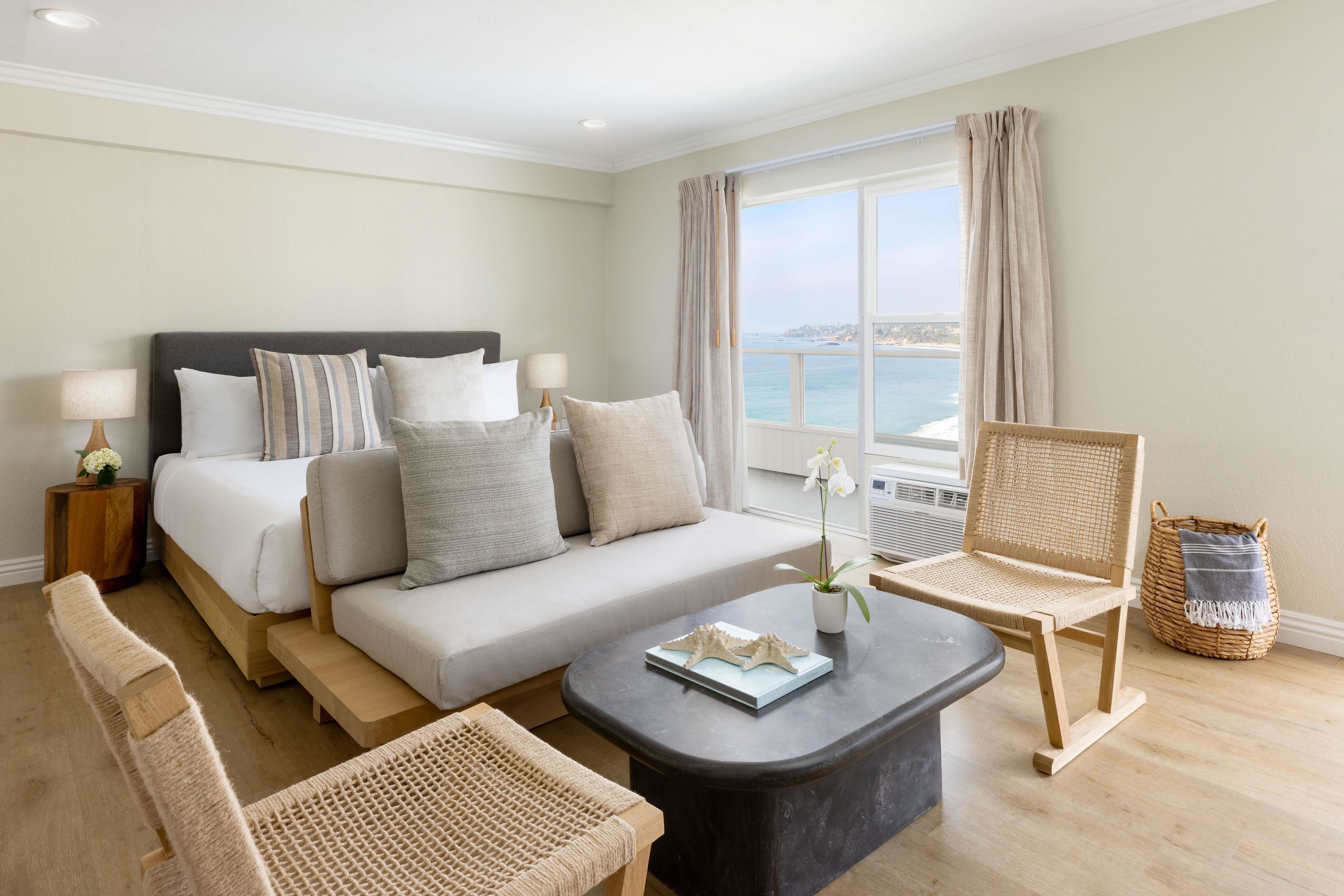 A hotel room with a bed, sofa, armchair, and a view of the sea.