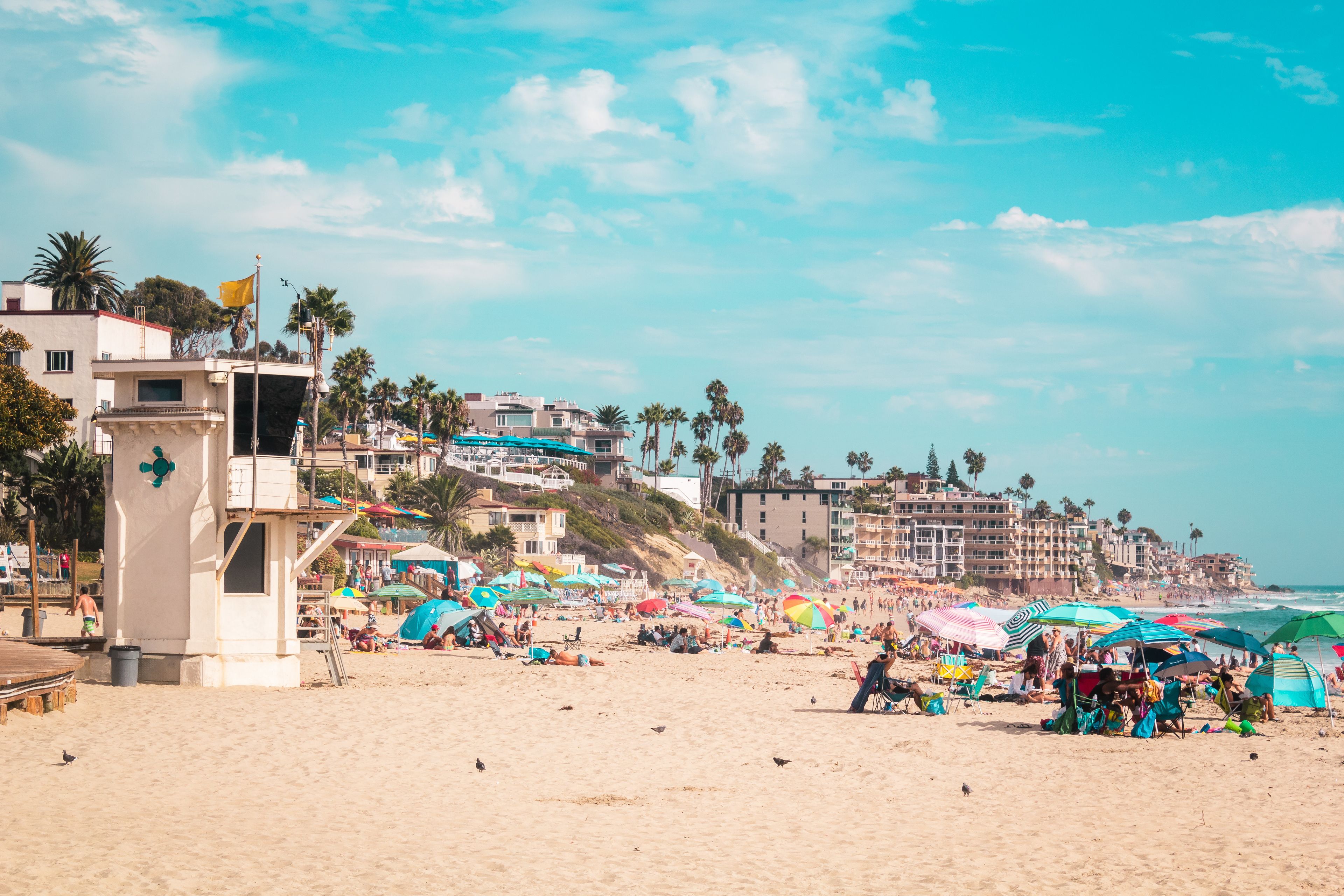Una playa con una torre de salvavidas, sombrillas y gente.