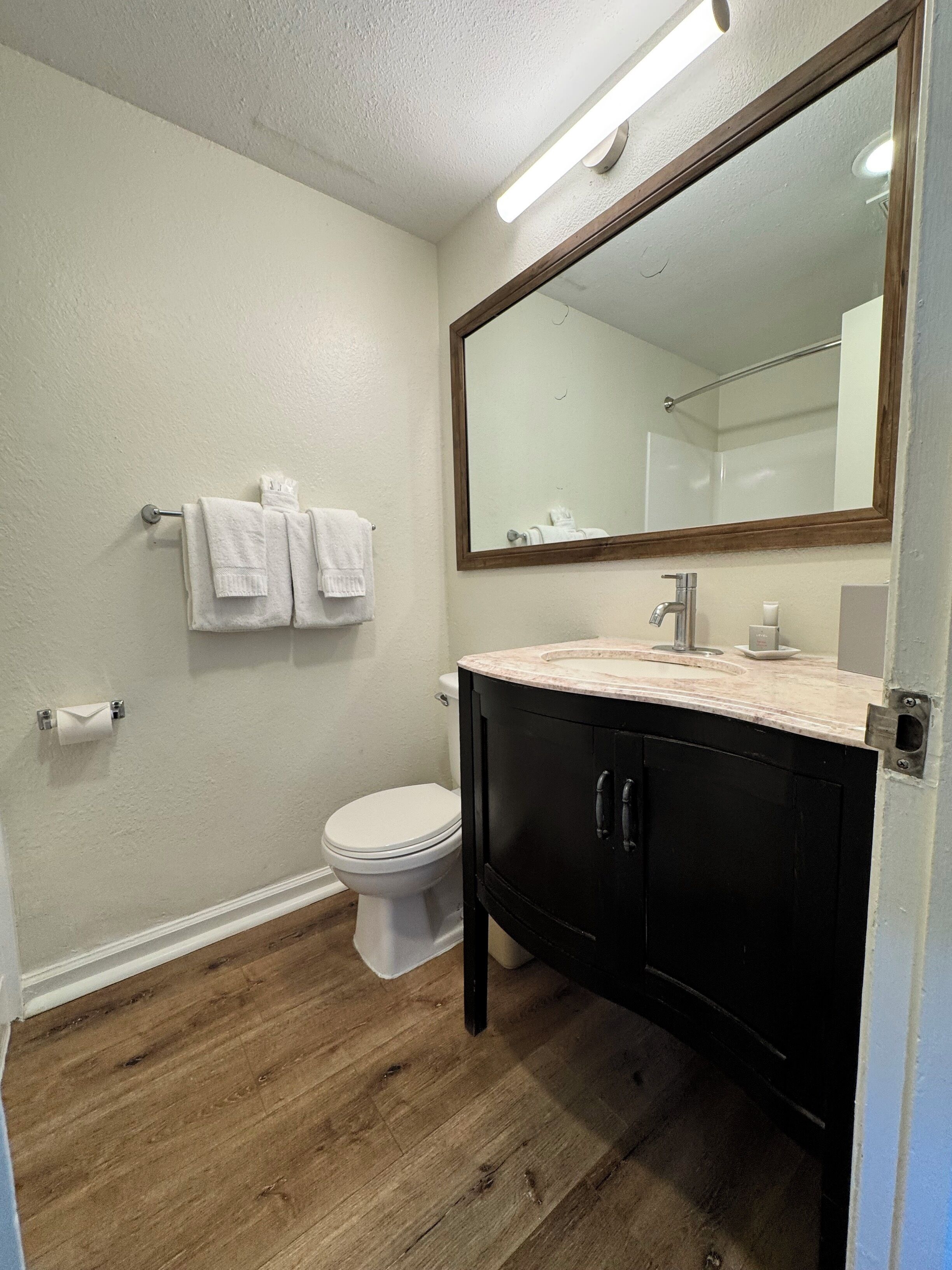 A bathroom with a white toilet, a black vanity with a mirror, and a towel rack with two white towels.