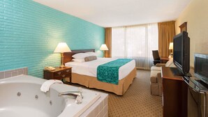 A hotel room with a large bed, a separate sofa, a desk with a TV, a desk lamp, a bathroom with a bathtub, and a window with curtains. - Howard Johnson by Wyndham Williamsburg (Williamsburg)