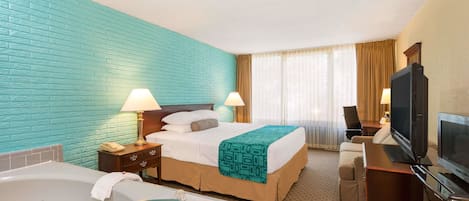 A hotel room with a large bed, a separate sofa, a desk with a TV, a desk lamp, a bathroom with a bathtub, and a window with curtains.