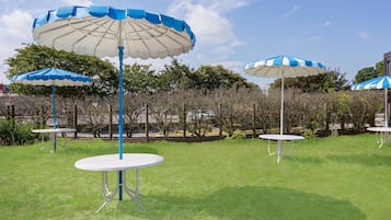 Un espacio al aire libre con césped, mesas redondas y sombrillas a rayas azules y blancas.
