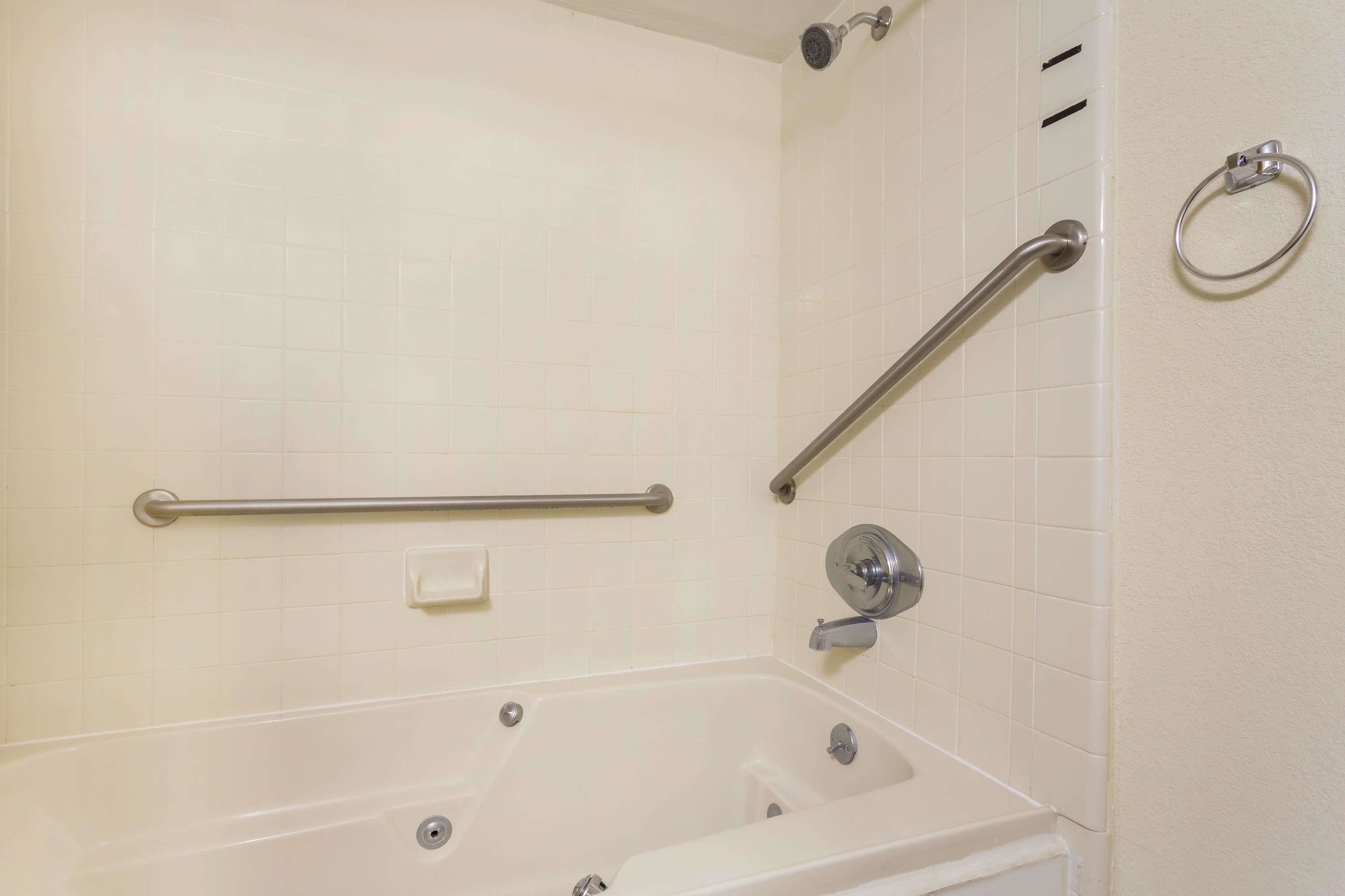 Un baño con bañera, barras de apoyo, argolla para toallas y jabonera.