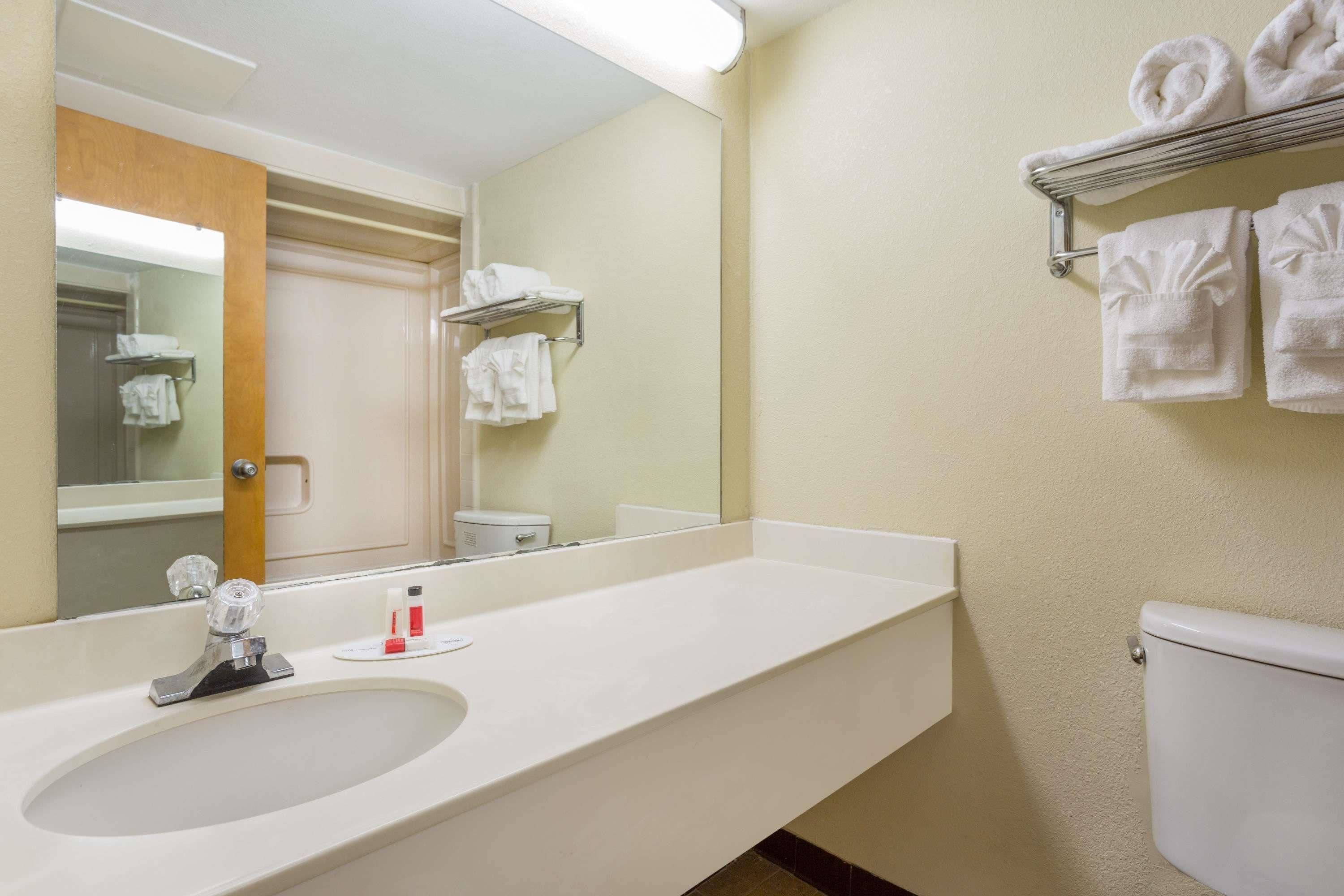 Un baño con lavamanos, espejo, toallero y retrete.