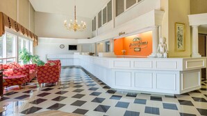 A hotel lobby with a check-in counter, a chandelier, and a seating area with red patterned sofas. - Howard Johnson by Wyndham Williamsburg (Williamsburg)