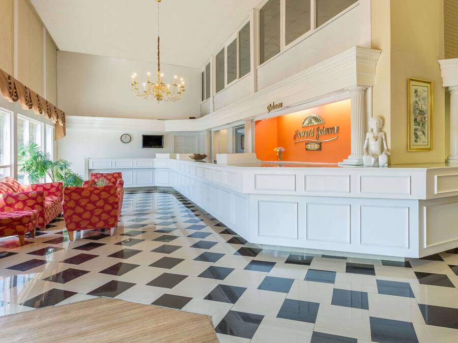 Eine Hotelhalle mit einer Rezeption, einer Chandelüster und einer Sitzecke mit roten Sofas mit Muster.
