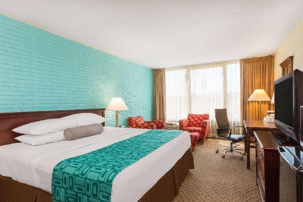 Una habitación de hotel con cama, escritorio, silla, televisor y ventana con cortinas.