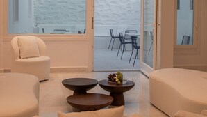 Un interior moderno con una lámpara circular en el techo, sofás blancos, una mesa de centro con fruta y vistas a una zona de estar exterior a través de amplios ventanales.