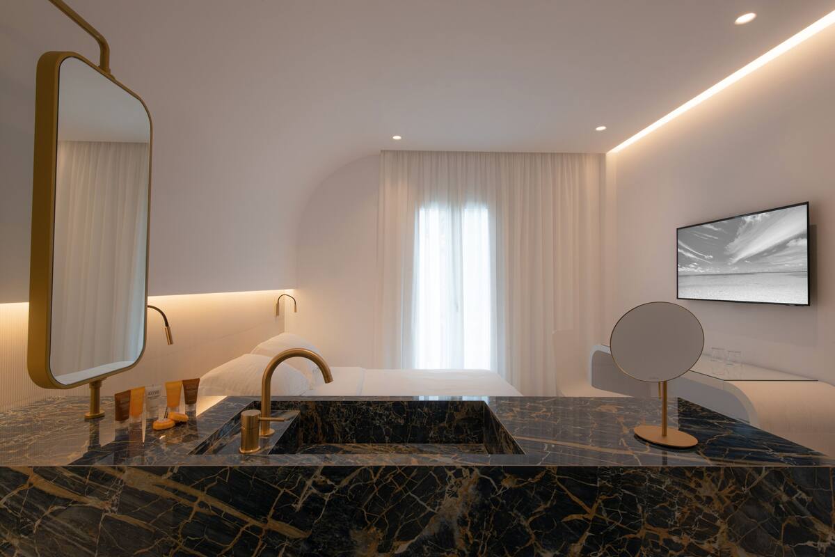 A modern bathroom with a marble sink, a large mirror, a bathtub, and a wall-mounted TV.