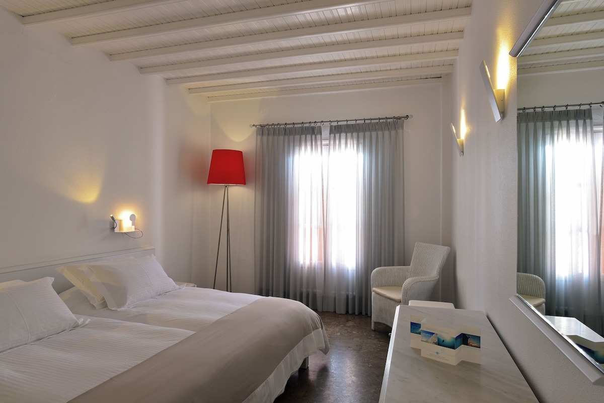 A hotel room with two beds, a red floor lamp, a chair, and a large mirror.