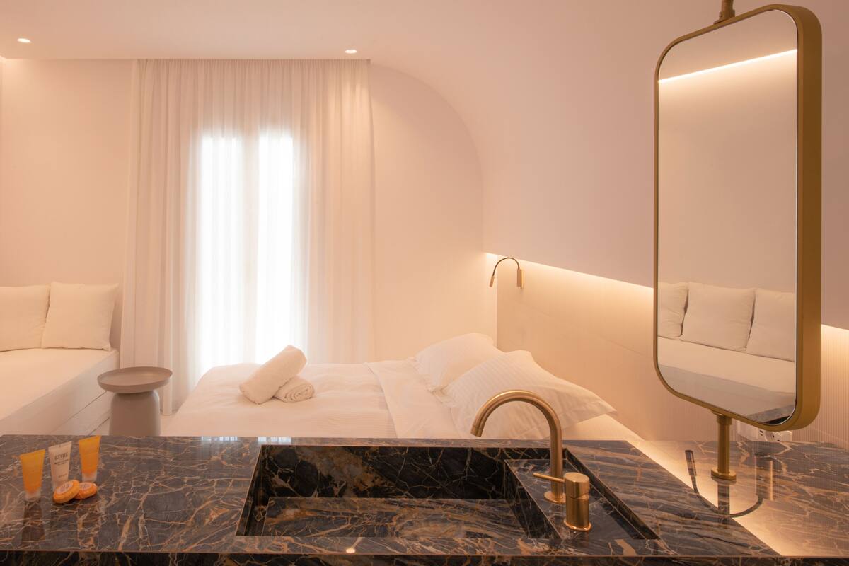 A modern hotel bathroom with a marble sink, a large mirror, and a bed with white linens.