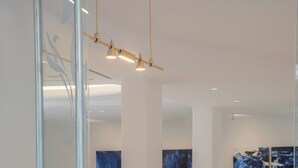 Un área de recepción moderna con un separador de vidrio, un mostrador blanco, una computadora portátil y arte abstracto en las paredes.