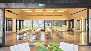 A spacious indoor area with tables and chairs arranged for dining, large windows offering views of the outdoors, and a ceiling with recessed lighting. - Voksenasen Hotell, BW Signature Collection (Oslo)