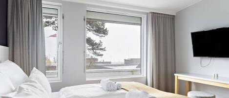 Une chambre d’hôtel avec un lit, une télévision, un bureau et une fenêtre avec des rideaux.