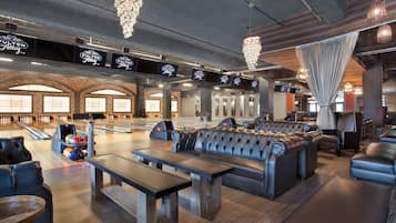 A bowling alley with multiple lanes, a seating area with leather couches, and overhead signs indicating lane numbers.
