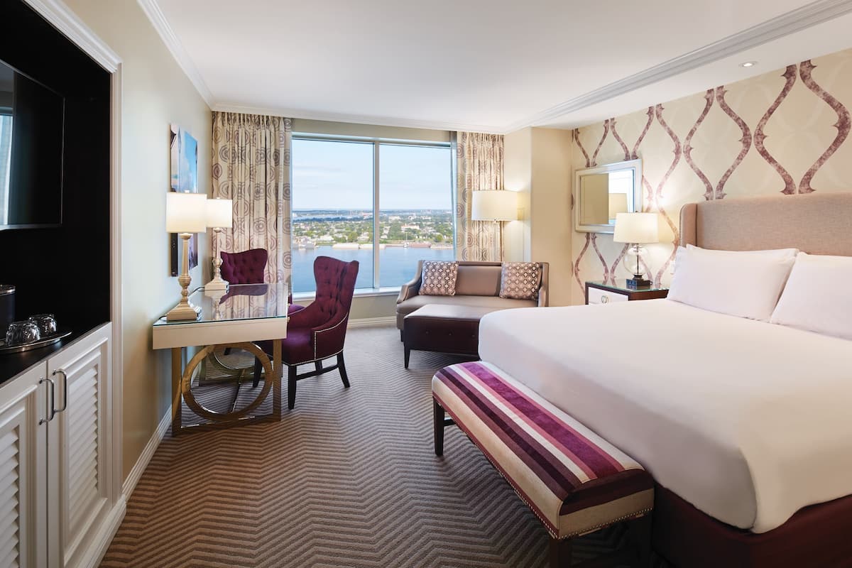 A hotel room with a large bed, a desk with a chair, a television, and a view of the city.