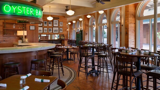 A restaurant interior with a bar area, wooden tables and chairs, and arched windows.