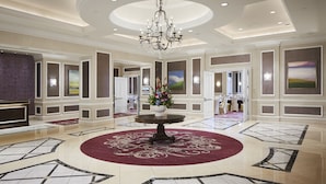 A spacious lobby with a central round table, a chandelier, and a floral arrangement.