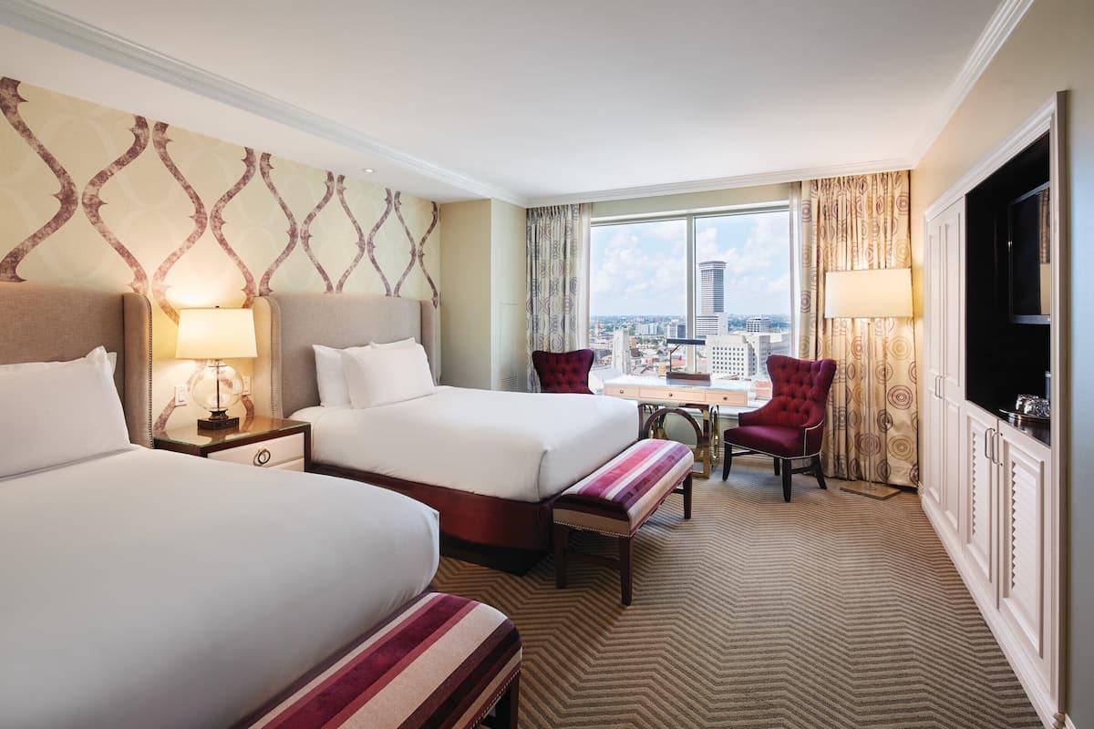 A hotel room with two beds, a desk, a chair, and a TV.