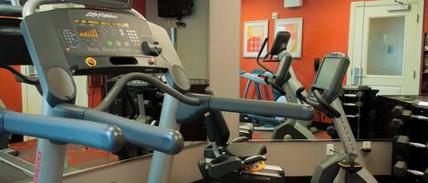A gym with cardio equipment, a clock, and a mirror.