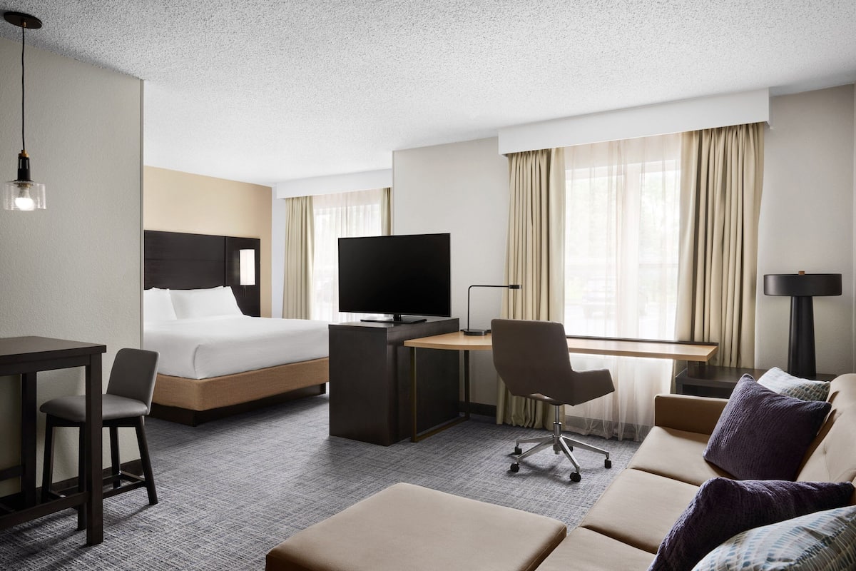 A hotel room with a bed, desk, TV, and seating area.