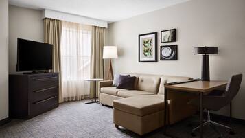 A hotel room with a flat-screen TV, a sofa, a desk, and a chair.