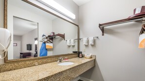 A bathroom with a granite countertop, a sink, a large mirror, and a towel rack. - Bryant Inn & Suites (Bryant)