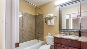 A bathroom with a bathtub, toilet, and shower. There is a vanity with a mirror and a towel rack above the sink. - Bryant Inn & Suites (Bryant)
