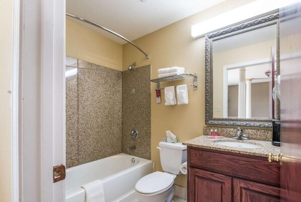 A bathroom with a bathtub, toilet, and shower. There is a vanity with a mirror and a towel rack above the sink.