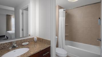 A modern bathroom with a granite countertop sink, a mirror, a toilet, and a bathtub.