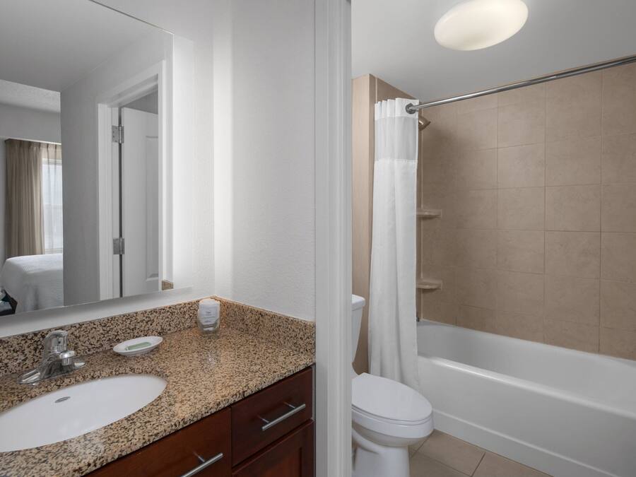 A modern bathroom with a granite countertop sink, a mirror, a toilet, and a bathtub.