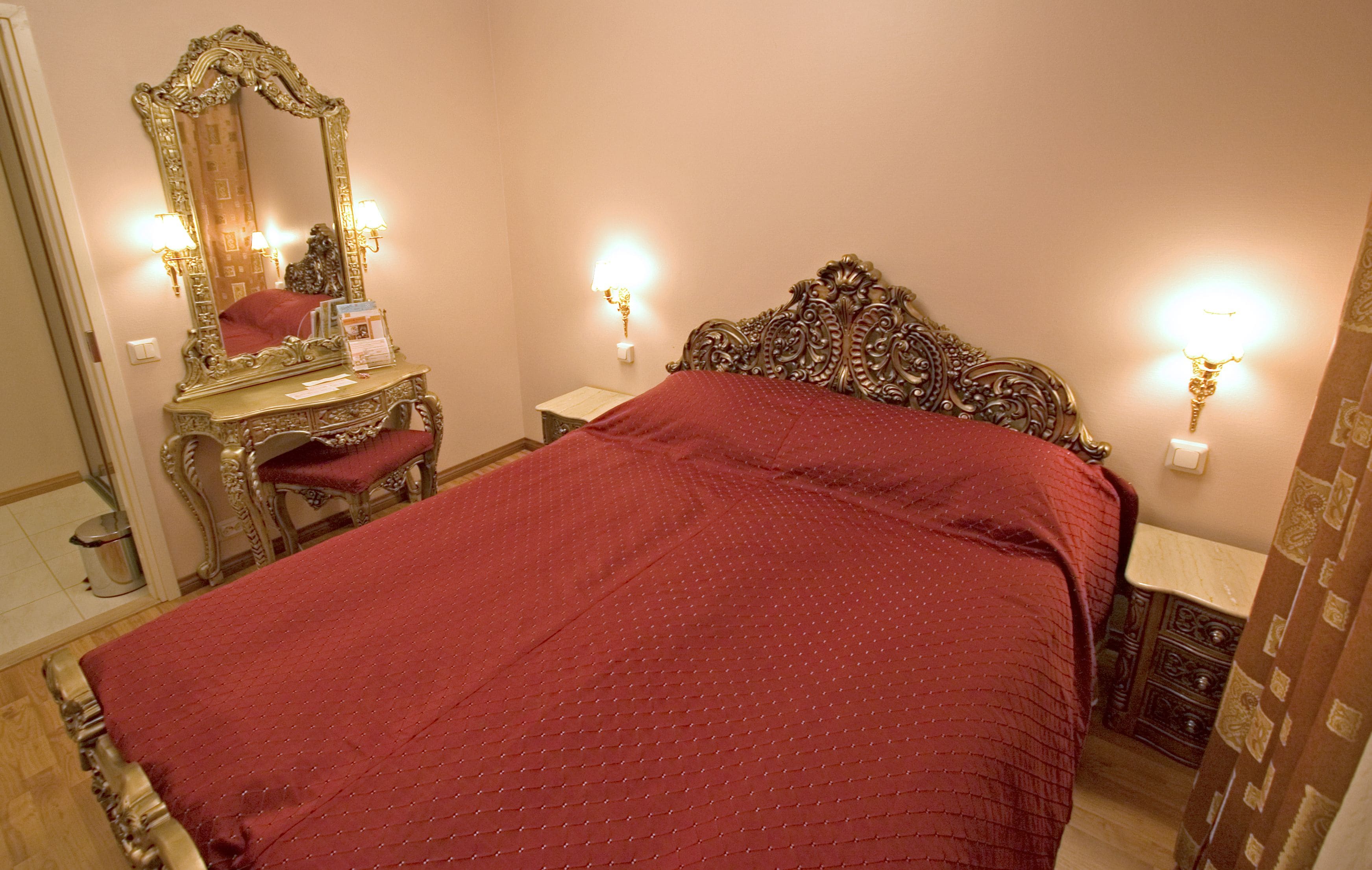 A bedroom with a large bed, a dresser, a mirror, and two wall sconces.