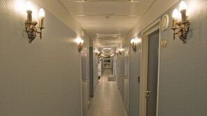 Hotellin käytävä, jossa on ovia molemmilla puolilla, seinissä valaisimia ja lattialla laatat.