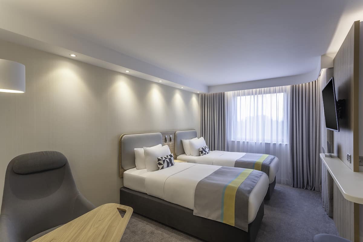 Une chambre d’hôtel avec deux lits, un bureau, une chaise et un téléviseur.