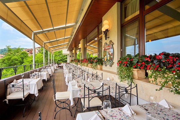 An outdoor dining area with tables set for guests, surrounded by potted plants and a view of the landscape.