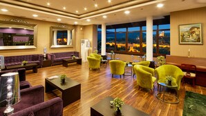 A spacious lobby with a wooden floor, a purple sofa, yellow armchairs, and a large window offering a view of a lit-up castle. - Yantra Grand Hotel -sharlopov Hotels (Veliko Tarnovo)