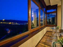 A balcony with a view of a town at dusk, a glass table with chairs, and a potted plant.