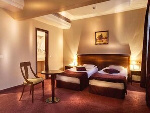Camera d'albergo con due letti, una sedia, un tavolino e un quadro appeso al muro.
