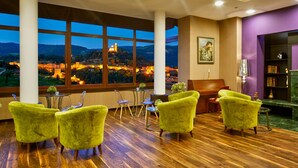 A room with large windows offering a view of a castle at dusk, wooden flooring, and bright green chairs. - Yantra Grand Hotel -sharlopov Hotels (Veliko Tarnovo)