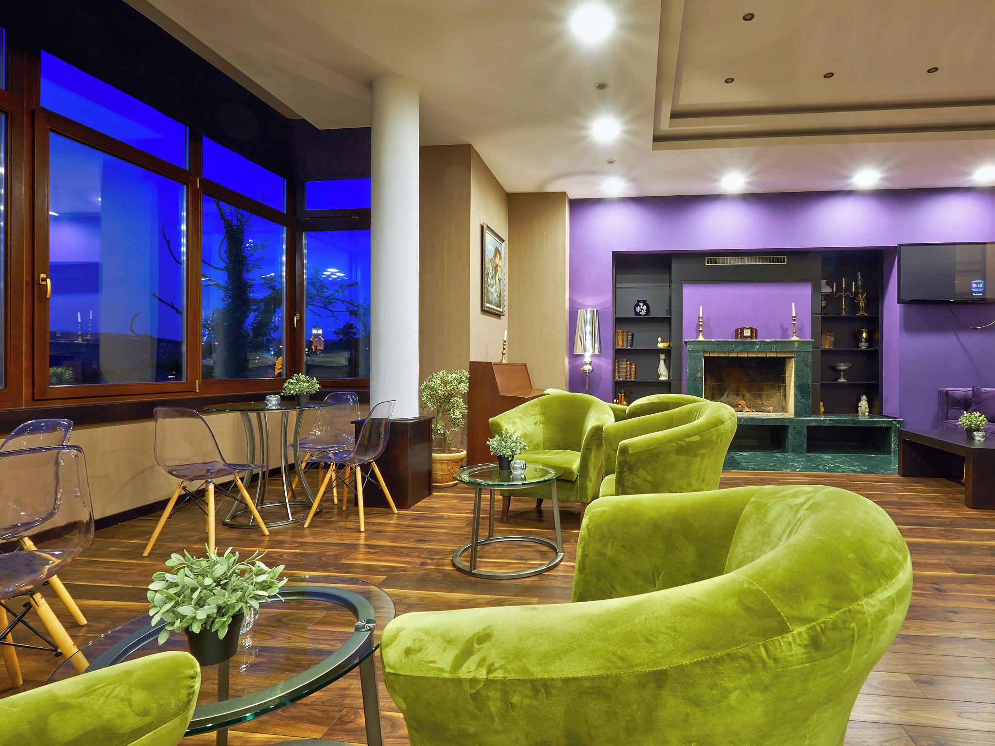 A modern lounge area with green upholstered chairs, a glass coffee table, and a fireplace.